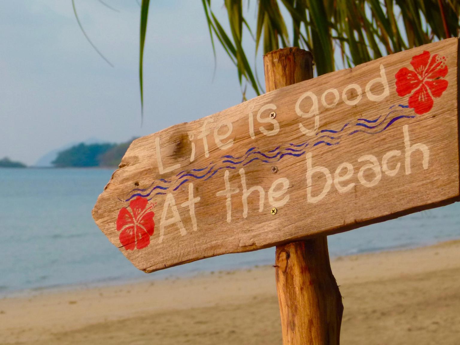 et treskilt på stranden i Thailand sier 'livet er godt på stranden'.
