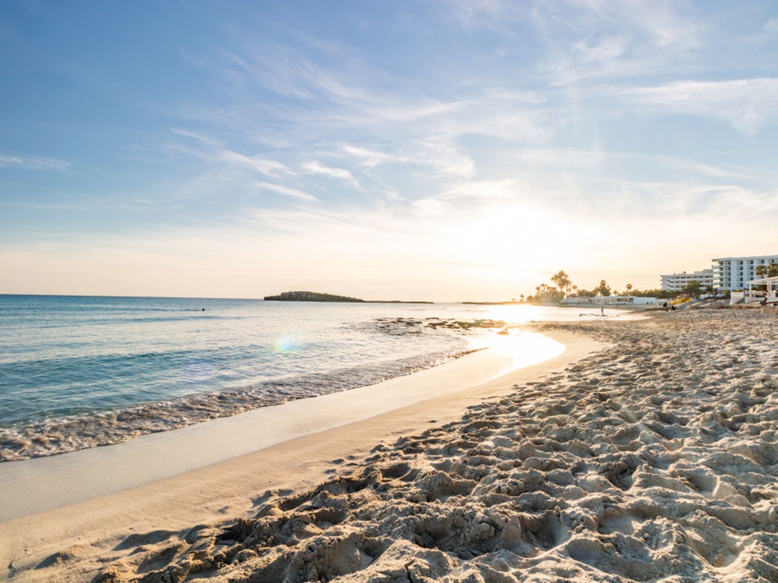 solen går ner över en sandstrand med ett hotell i bakgrunden.