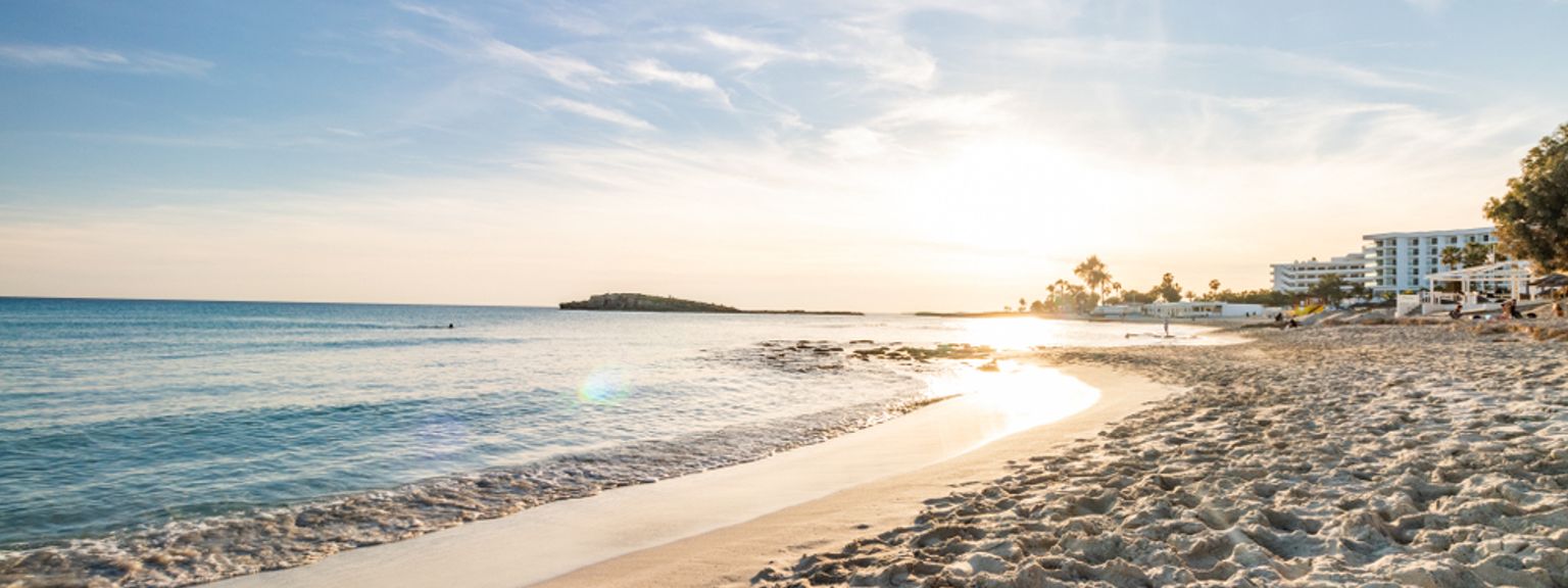 solen går ner över en sandstrand med ett hotell i bakgrunden.