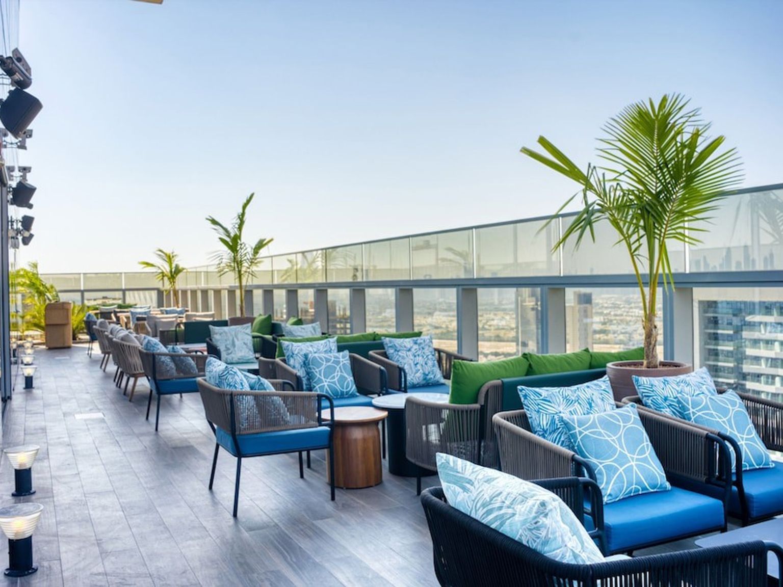 Moderne takterrasselounge med blå og grønne polstrede sitteplasser, palmer og utsikt over byens skyline.
