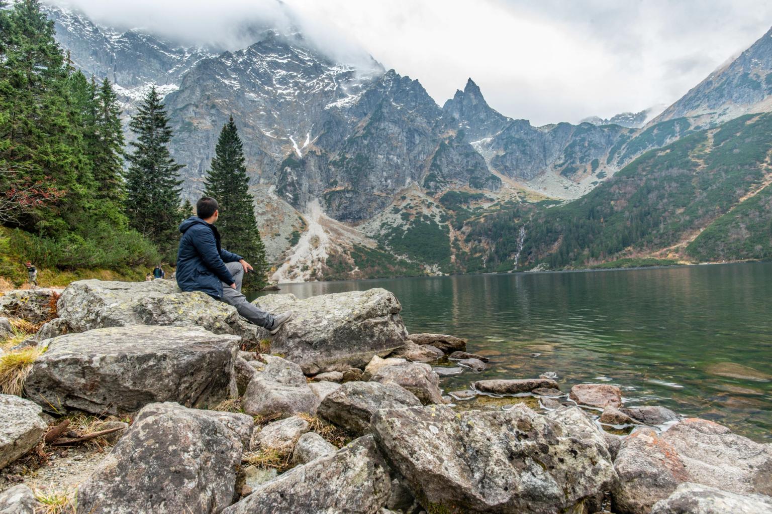 en mand sidder på en sten nær en sø i bjergene