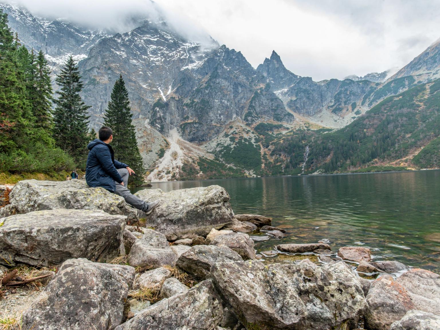 en man sitter på en sten nära en sjö i bergen