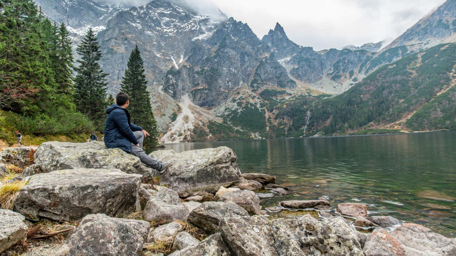 en mand sidder på en sten nær en sø i bjergene