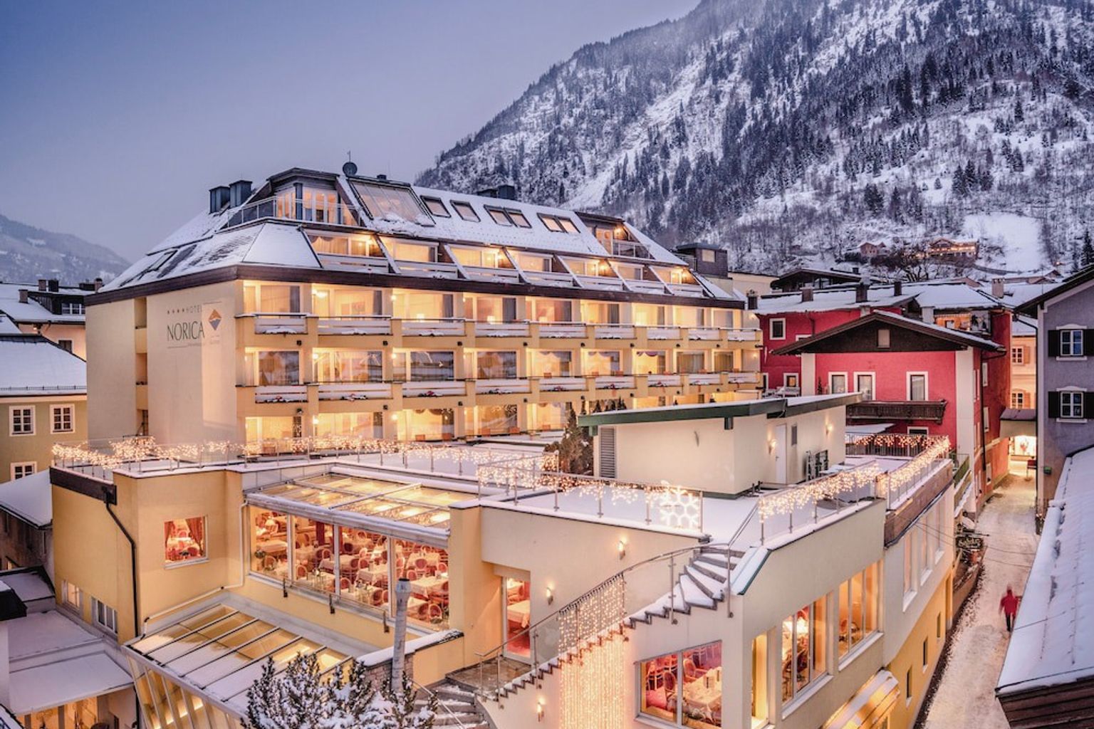 een groot gebouw met veel ramen is omgeven door sneeuw en bergen, Hotel Norica THERME, Bad Hofgastein