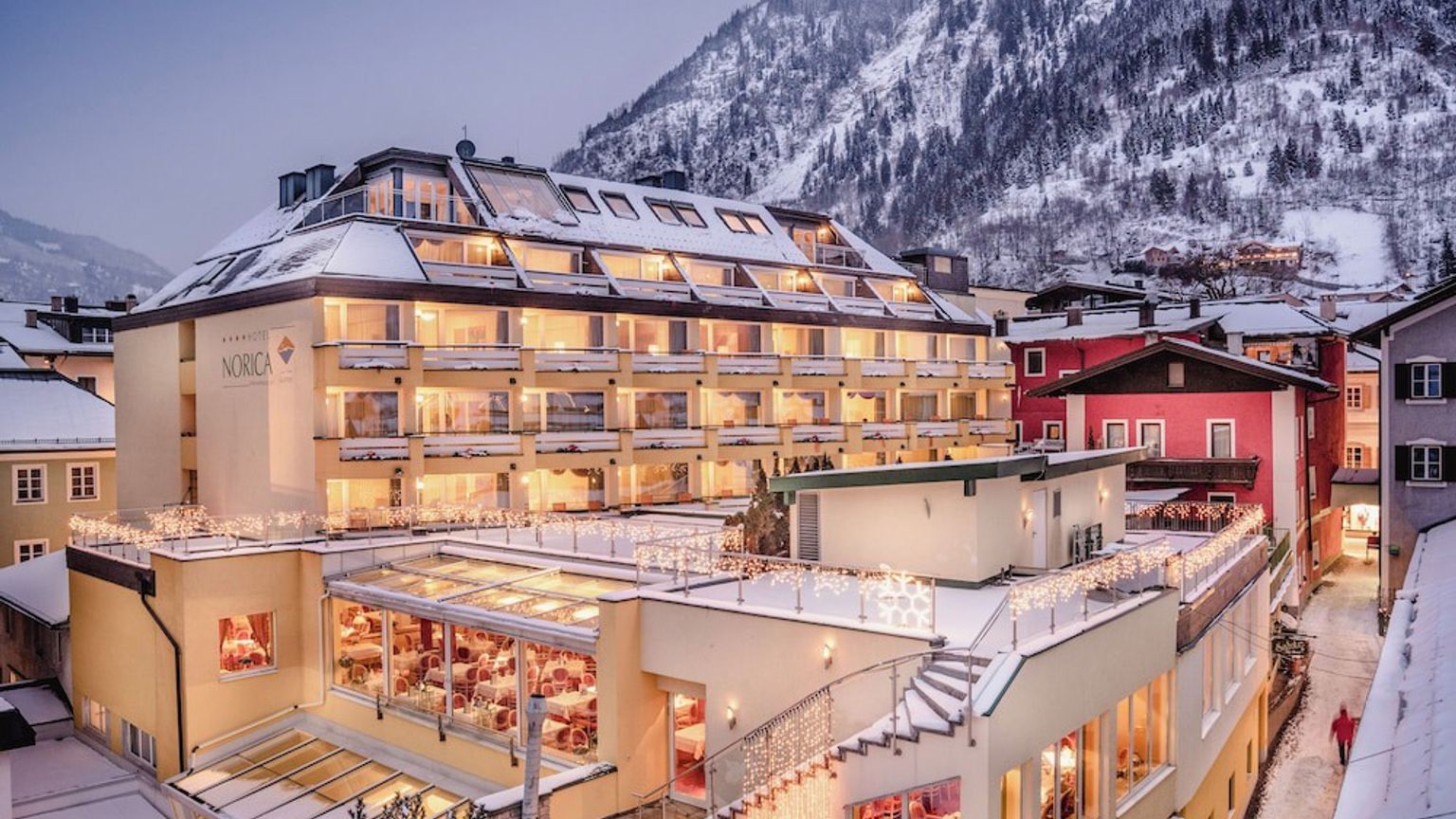 een groot gebouw met veel ramen is omgeven door sneeuw en bergen, Hotel Norica THERME, Bad Hofgastein