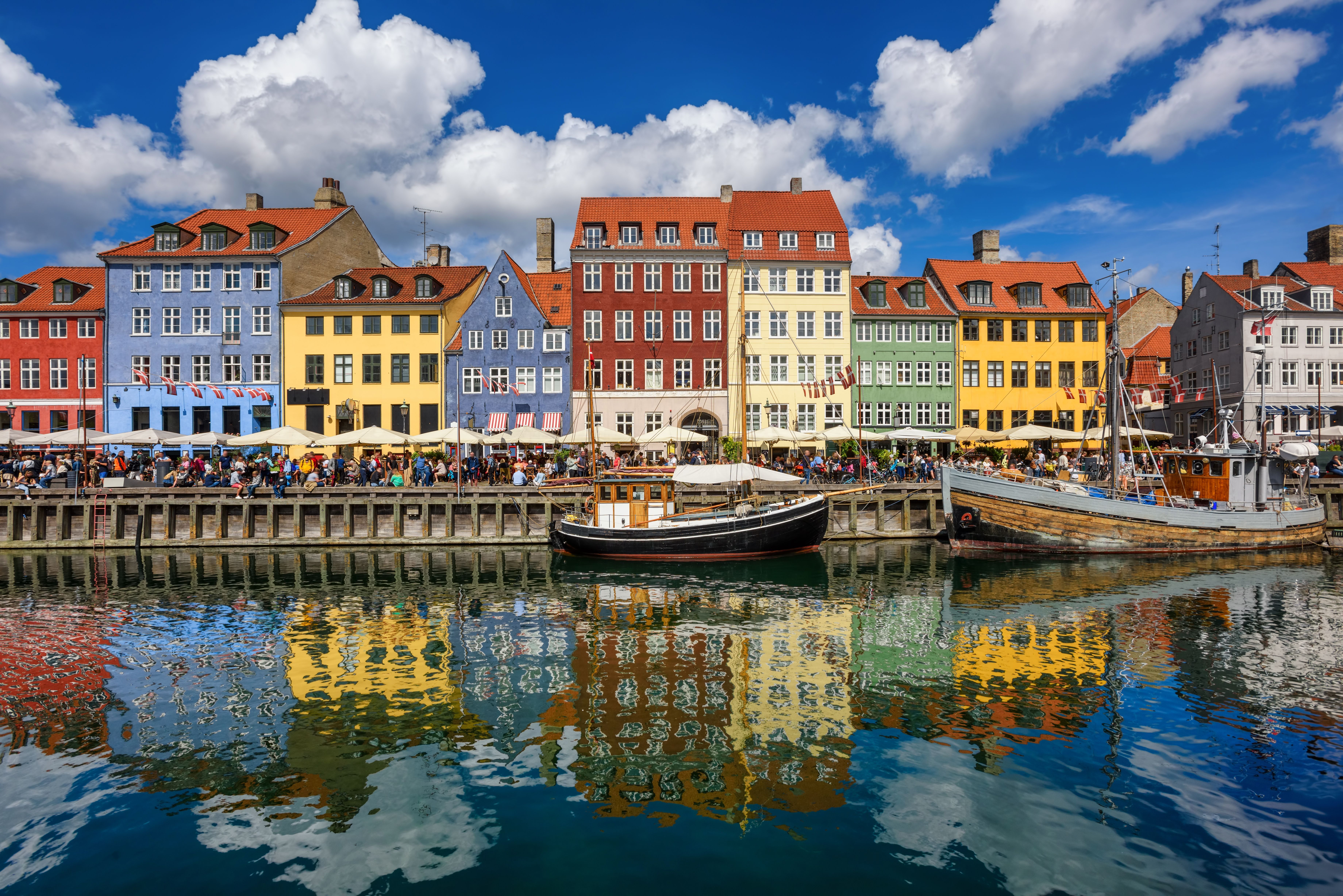 Färgglada byggnader längs Nyhavns kanal i Köpenhamn, med båtar och människor som äter.