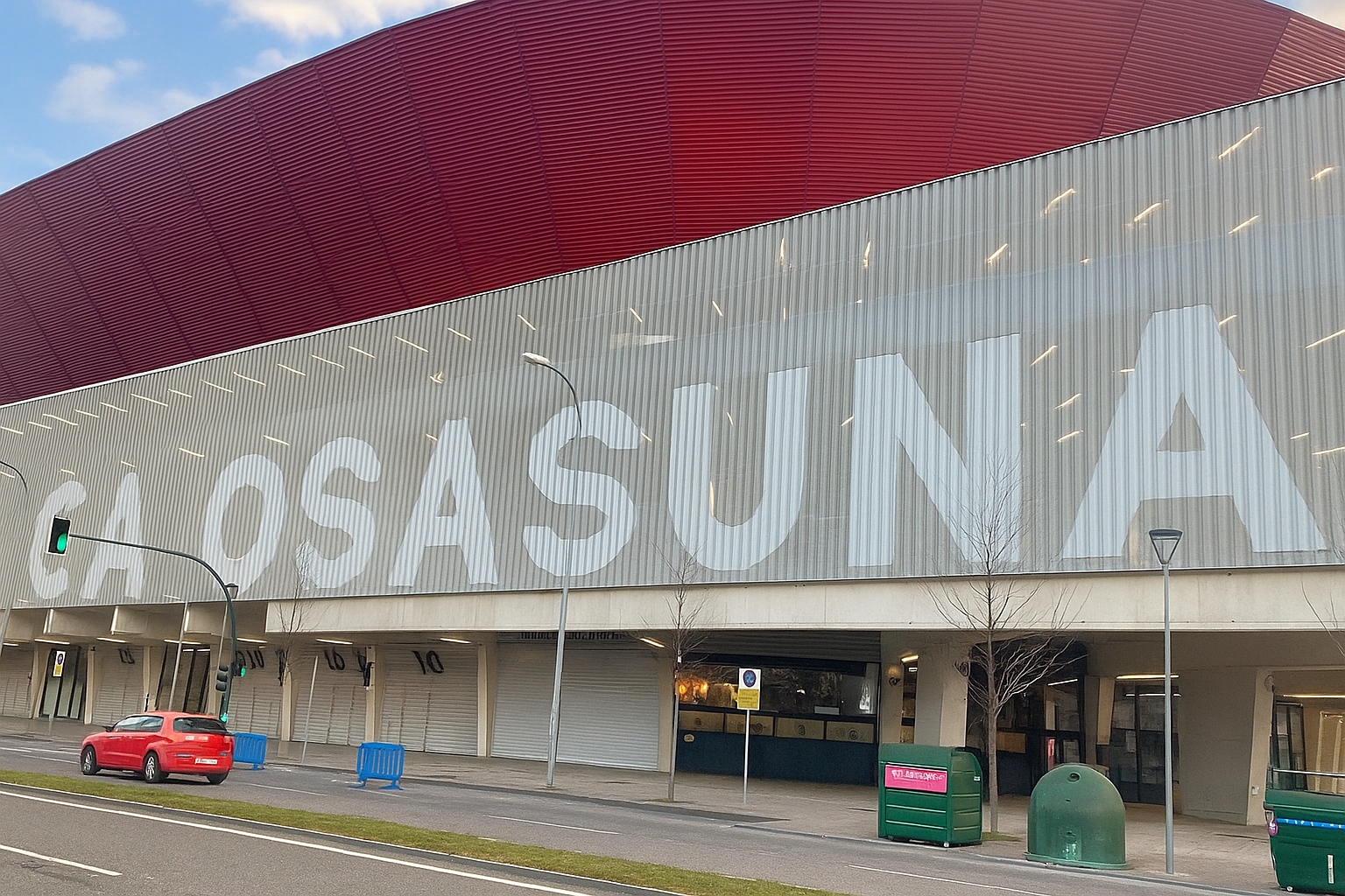 A stadium with a red roof and "CA OSASUNA" written in large white letters on its gray facade, seen from a street.