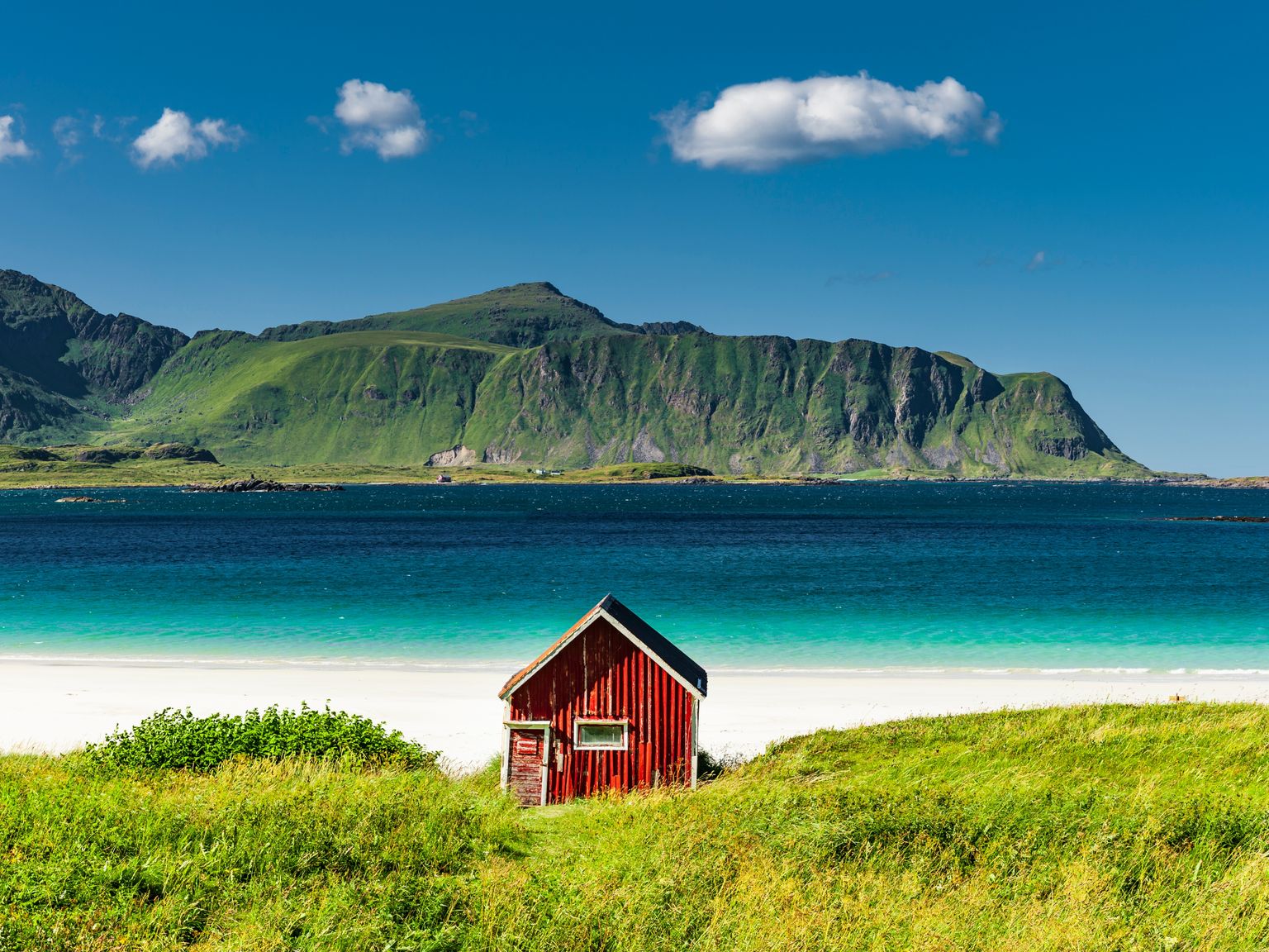 ein kleines rotes Haus sitzt am Ufer eines Strandes