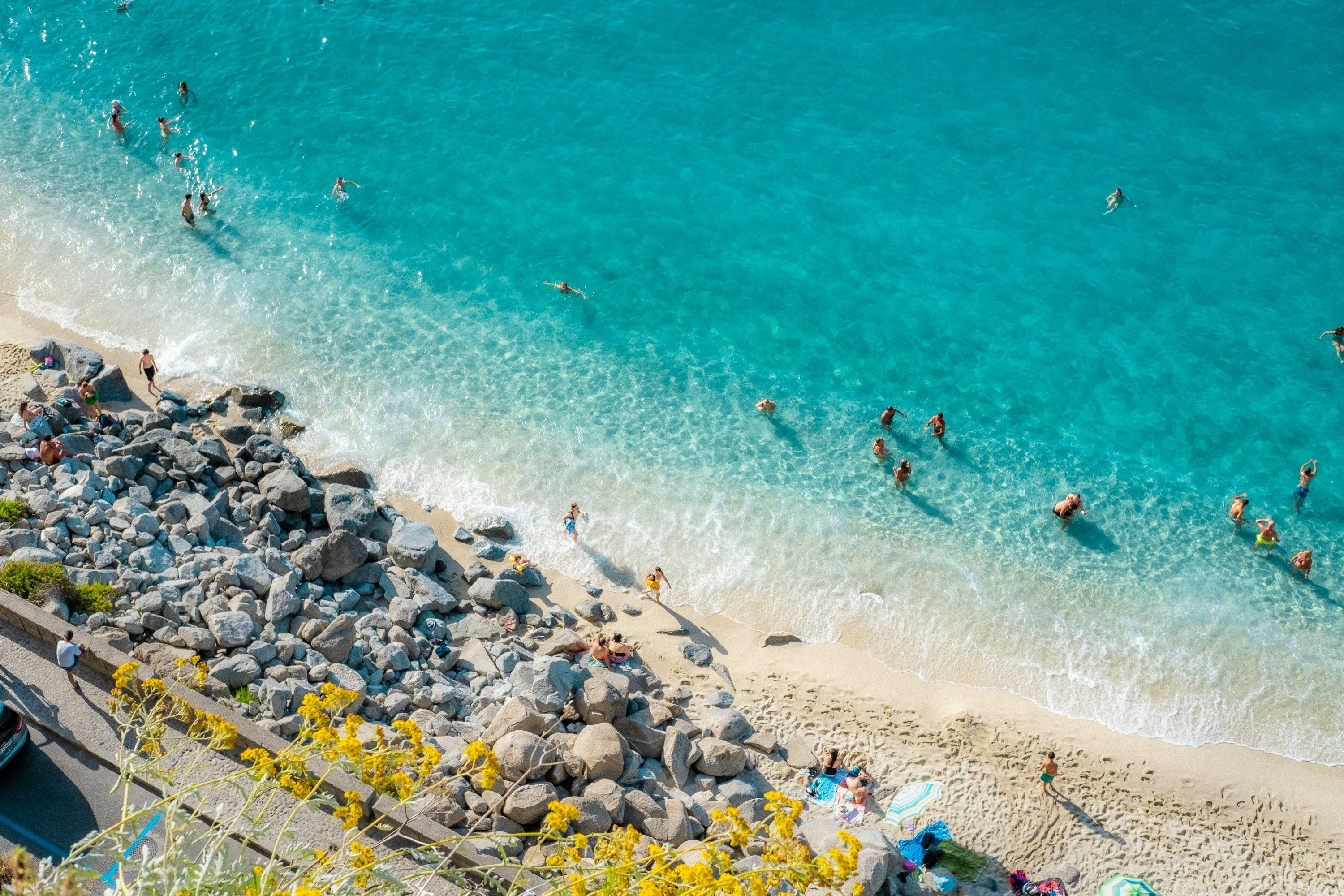 Flyfoto av en livlig strand med klart turkis vann, folk som svømmer og solbadere. Calabria, Italia