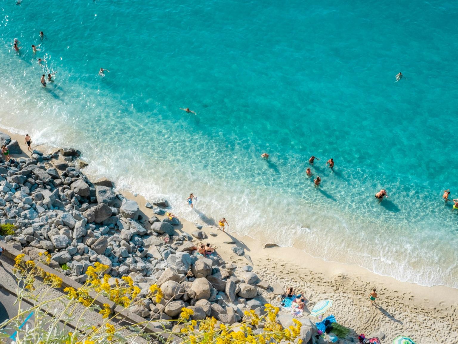 Veduta aerea di una spiaggia vivace con acqua turchese cristallina, persone che nuotano e bagnanti al sole. Calabria, Italia