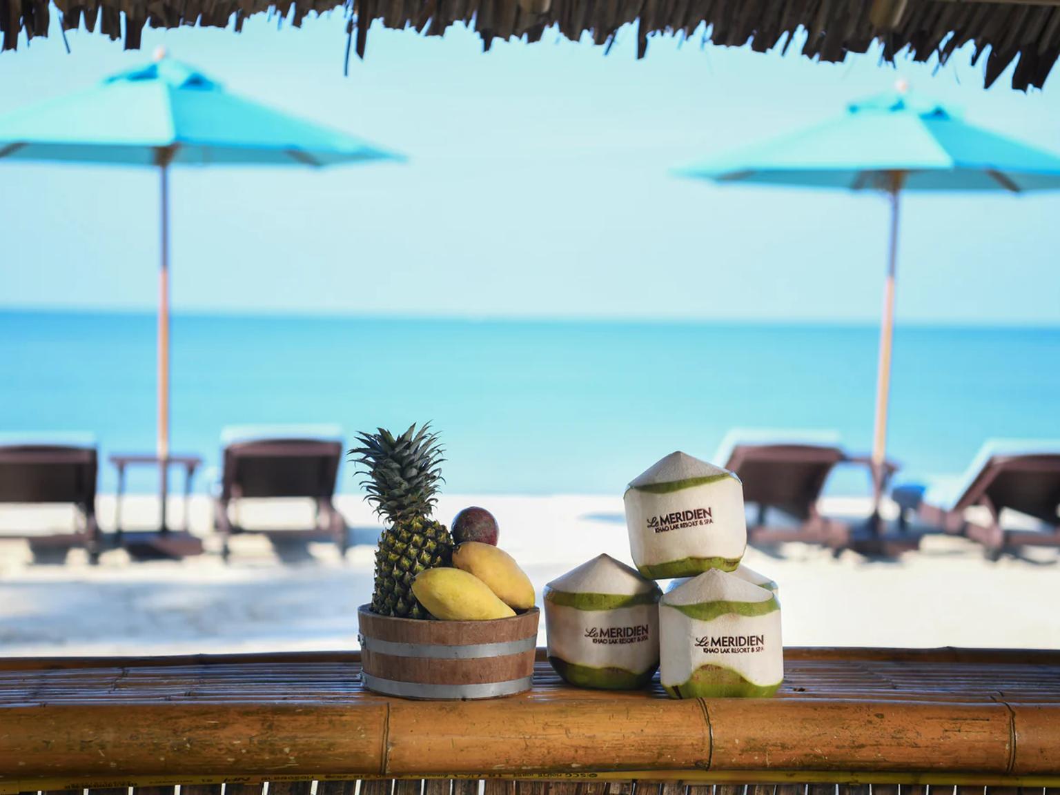 a bar with fruit and coconuts on it and umbrellas on the beach.