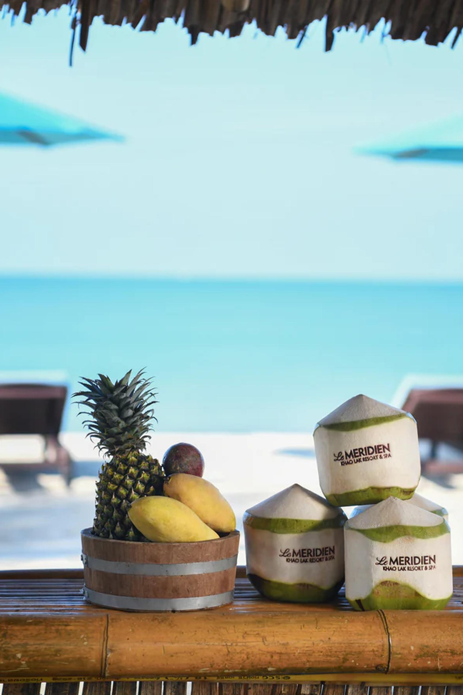 a bar with fruit and coconuts on it and umbrellas on the beach.