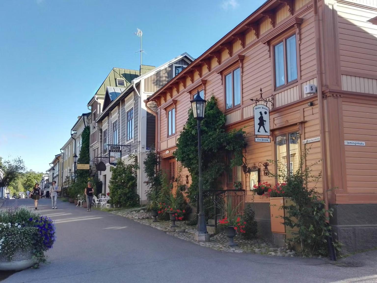 A street lined with traditional colorful wooden buildings under a clear blue sky, with a few people walking.