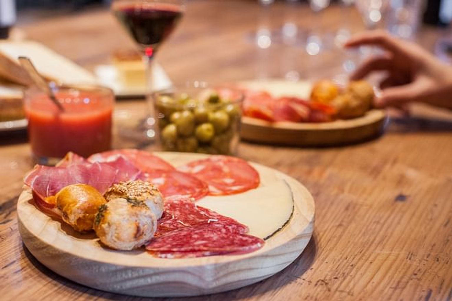 en träplatta toppad med kött och ost på ett träbord. Tapas