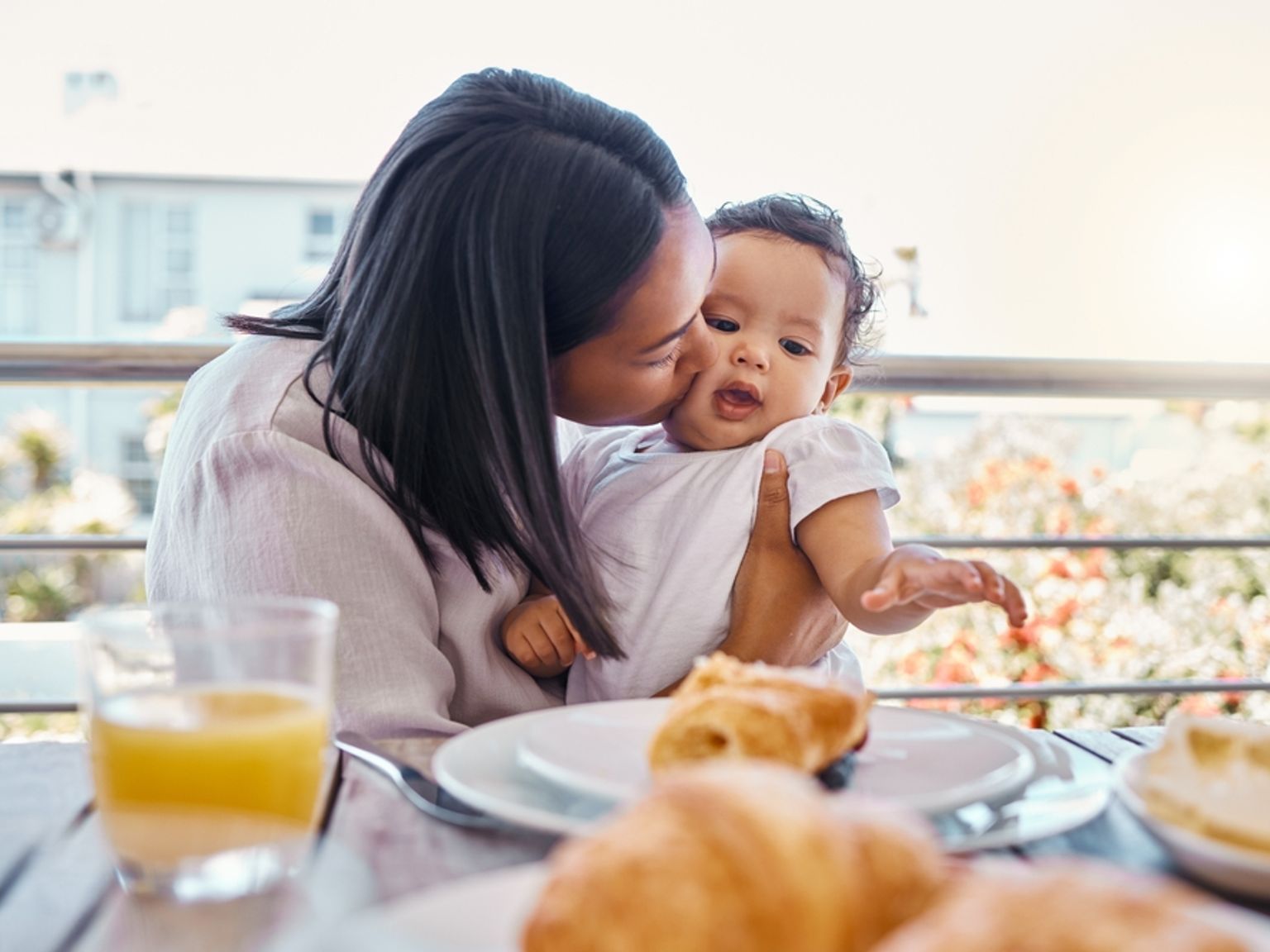 une femme tient un bébé tout en étant assise à une table avec une assiette de nourriture.