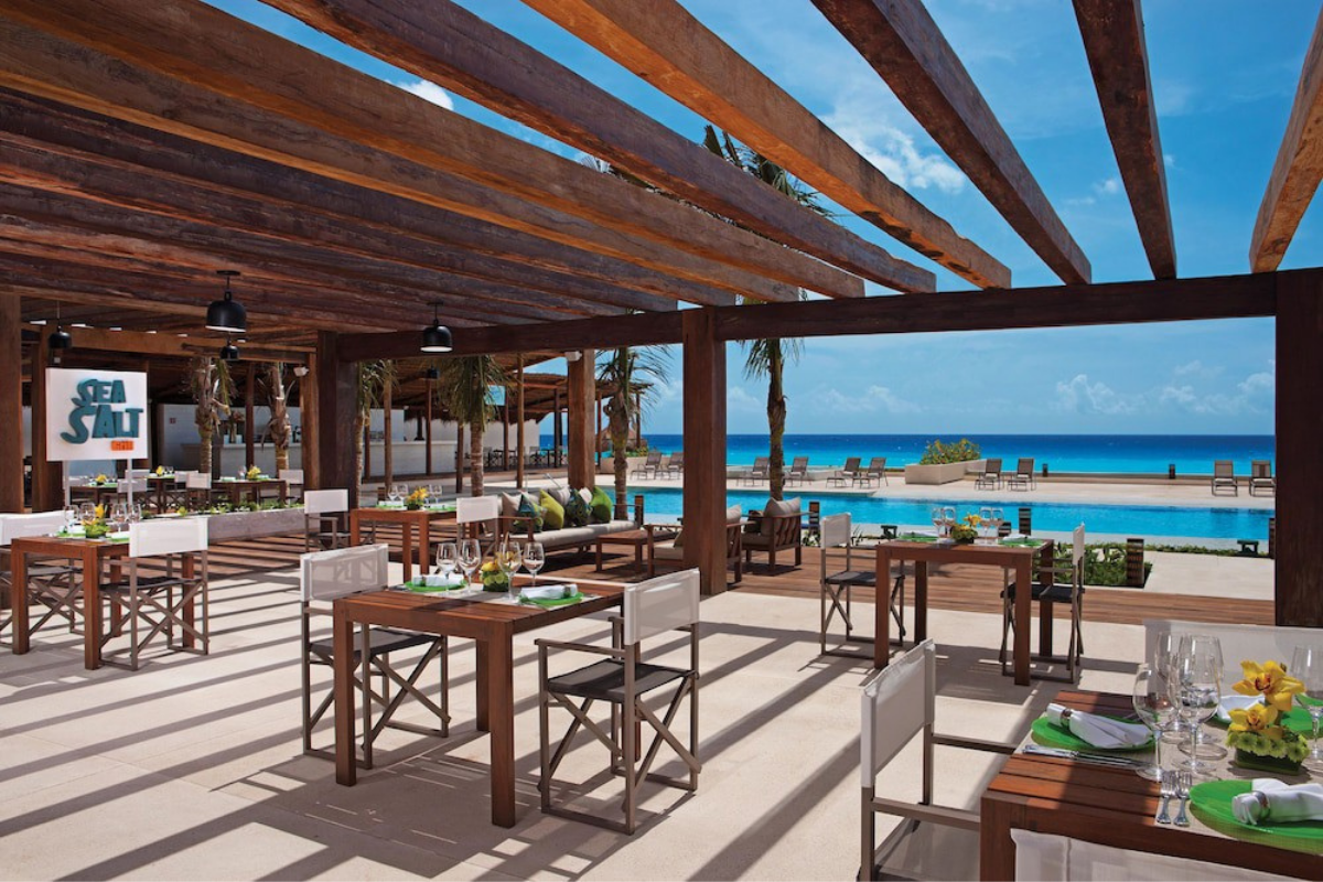 Restaurant en plein air « Sea Salt » sous une pergola en bois, avec vue sur une piscine et l’océan.