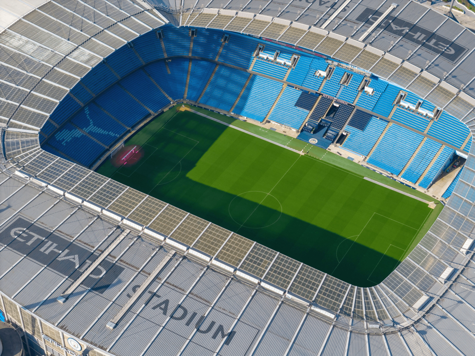 Vue aérienne du stade Etihad avec un terrain vert et des sièges bleus.