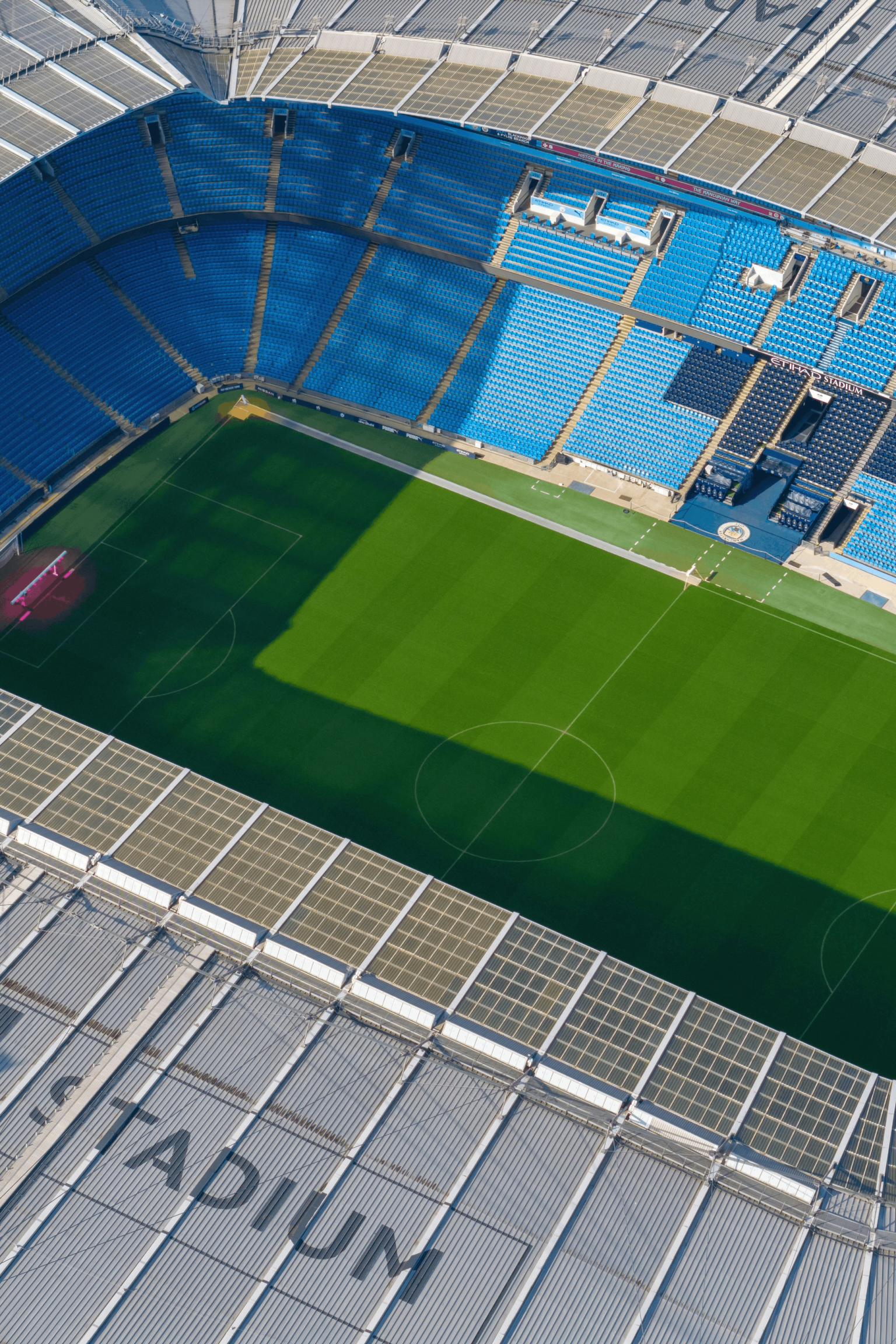Vue aérienne du stade Etihad avec un terrain vert et des sièges bleus.