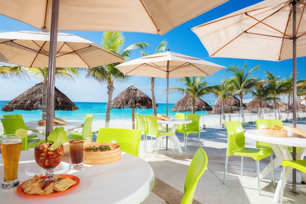 Utomhus strandrestaurang med mat och dryck, limegröna stolar, parasoller, palmer och en turkos ocean.