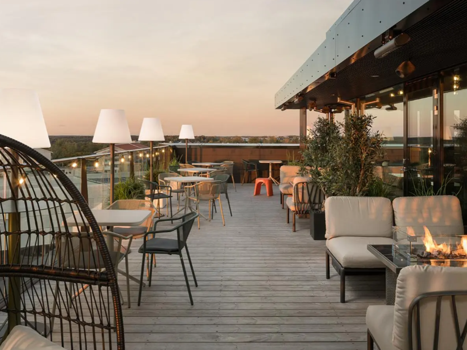 Moderni kattoterassi, jossa on oleskelu- ja ruokailualueet, tulisija ja valoketjut auringonlaskun aikaan.