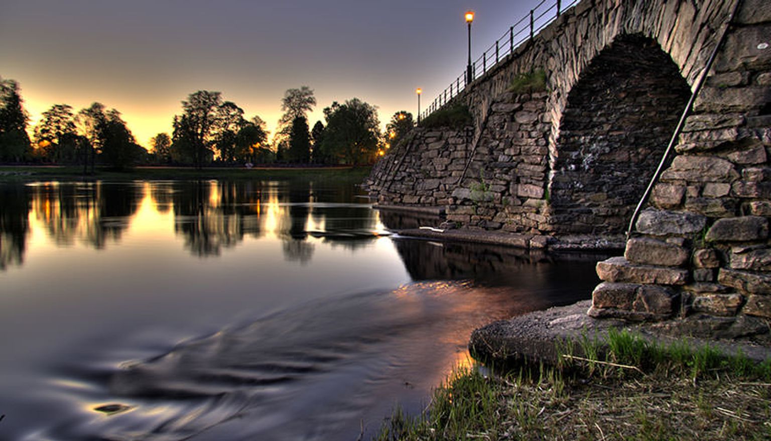 en stenbro over en flod med en solnedgang i baggrunden