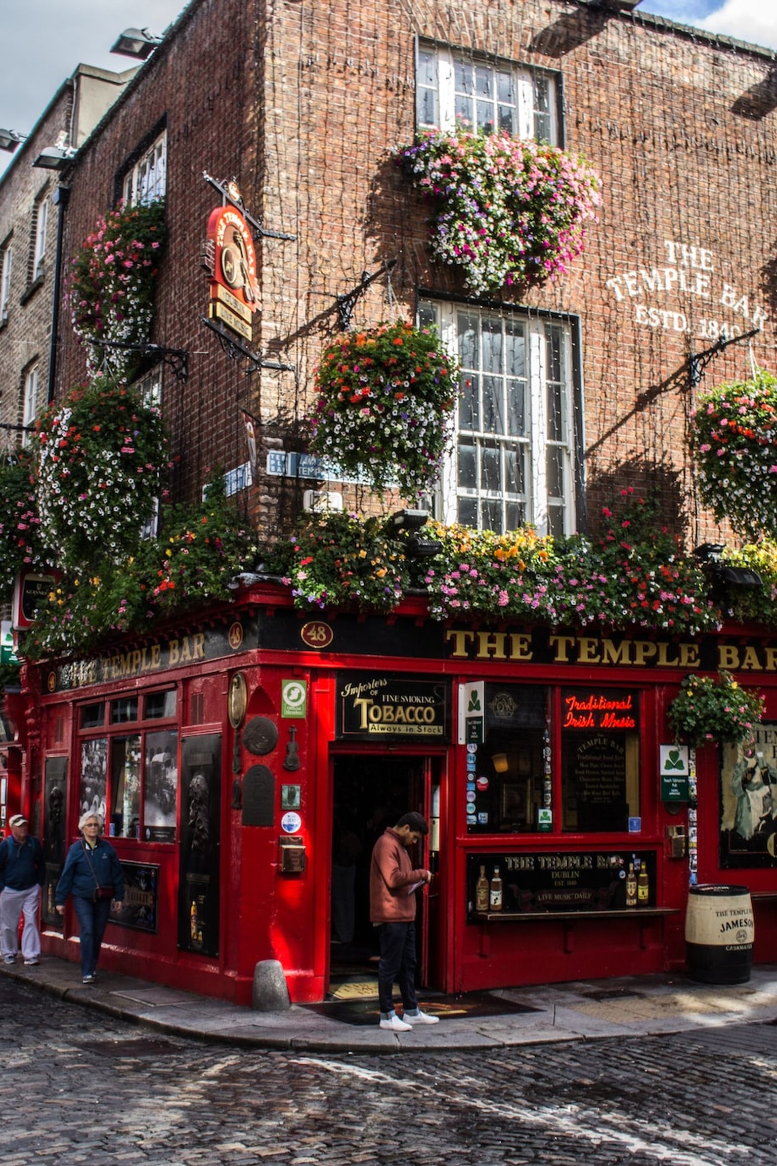 ryhmä ihmisiä kävelee mukulakivikadulla punaisen rakennuksen edessä, Dublin