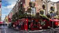 a group of people are walking down a cobblestone street in front of a red building, Dublin