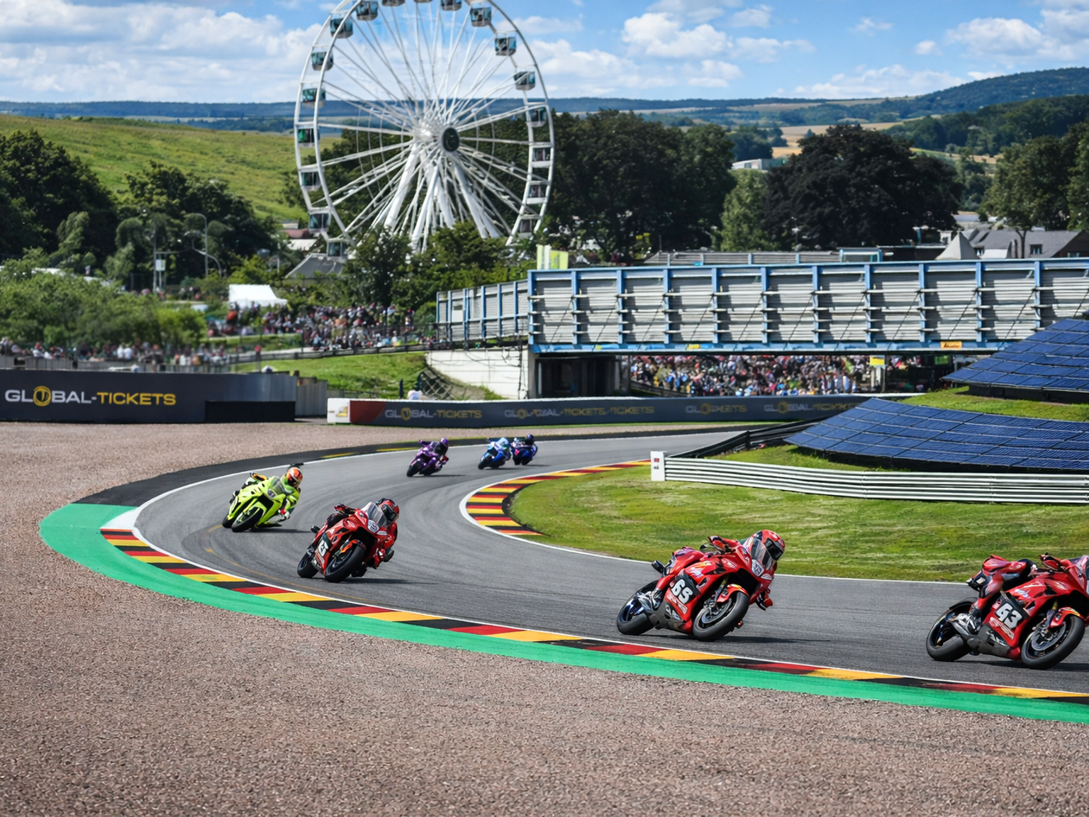 Motorcycles race on a track with German flag curbs, a Ferris wheel, and spectators.