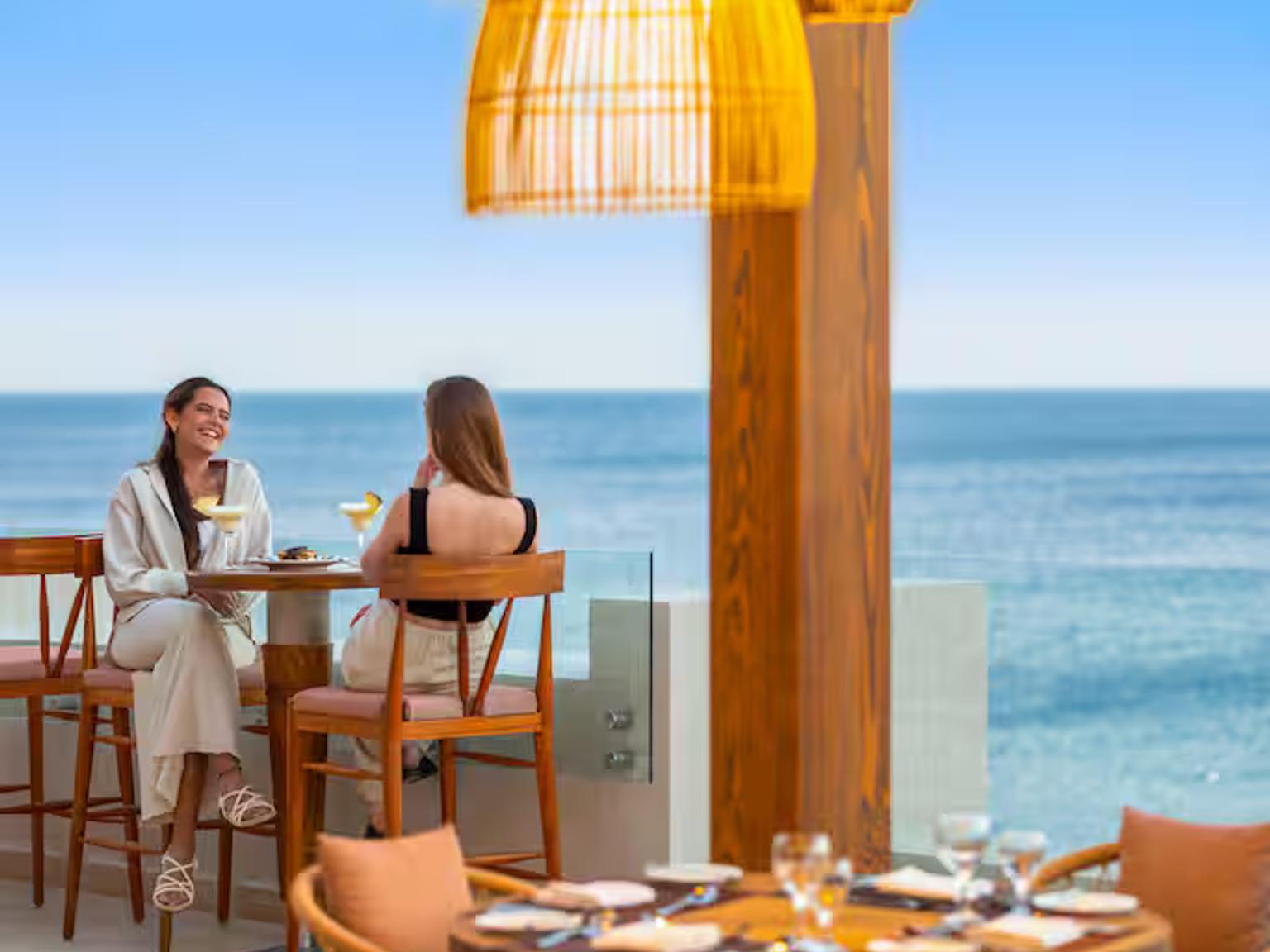 two women are sitting at a table with a view of the ocean.
