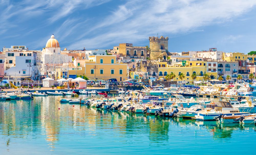 Port rempli de bateaux dans une ville côtière colorée avec une église à dôme et une tour en pierre. Ischia, Italie