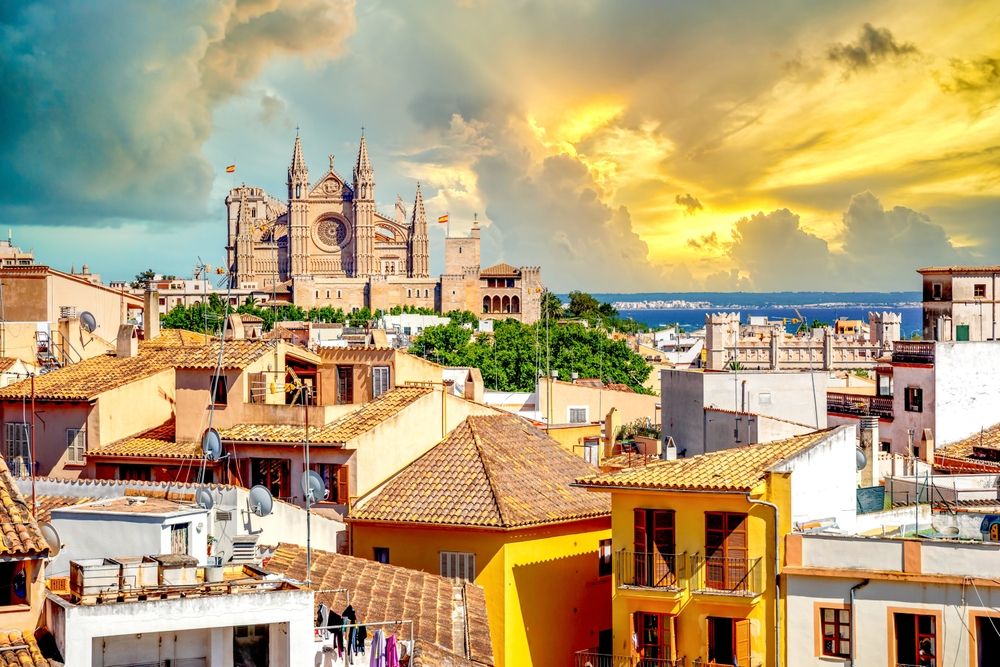 La Seu Cathedral overlooking Palma de Mallorca's terracotta rooftops and the sea under a dramatic golden sky.