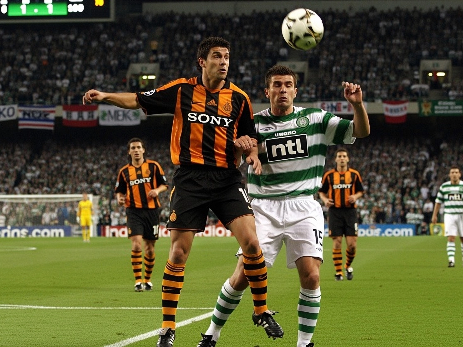 Två fotbollsspelare, en i orange och svart, en i grönt och vitt, kämpar om en luftboll.