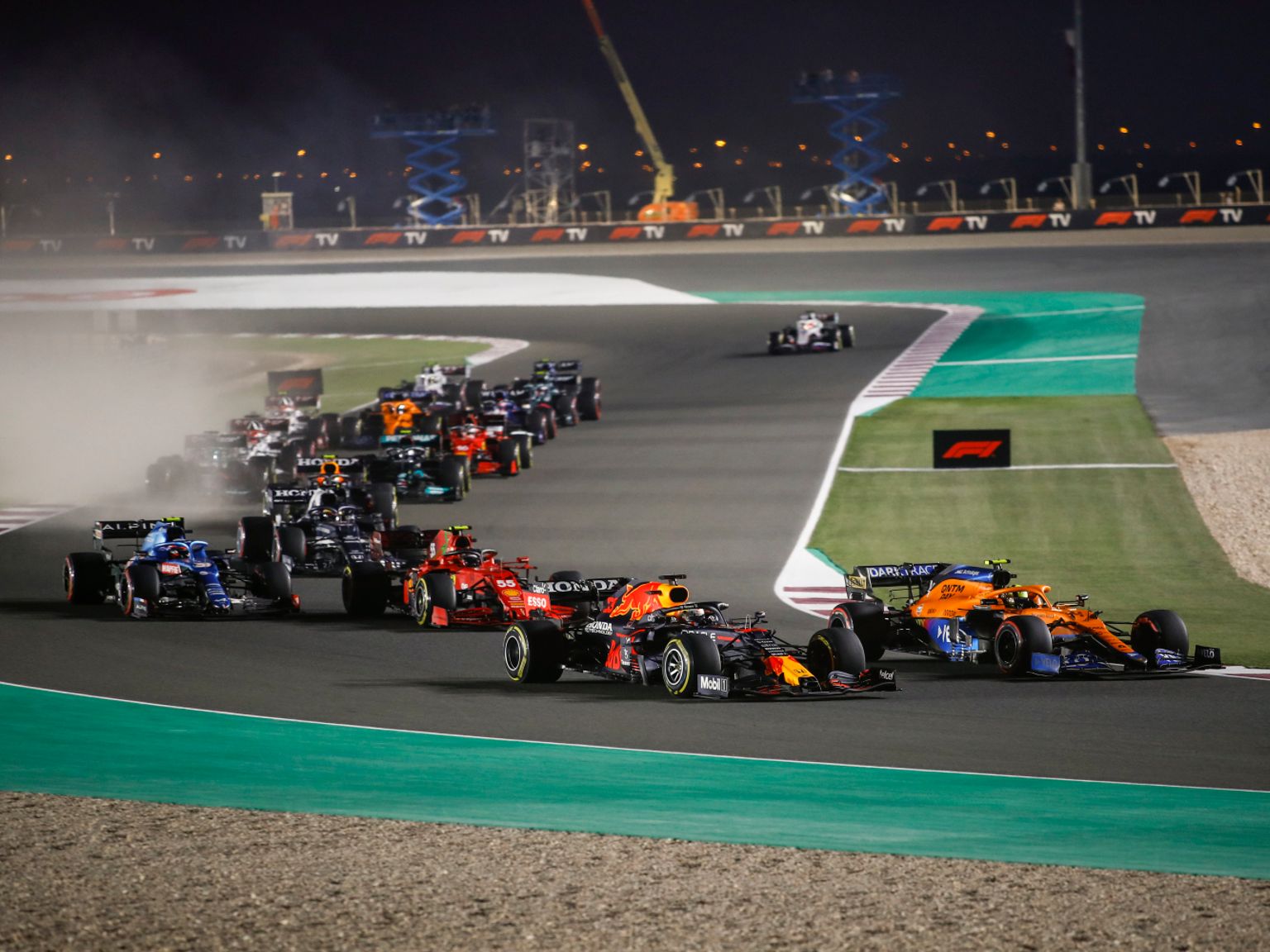 A pack of Formula 1 cars racing at night on a track.