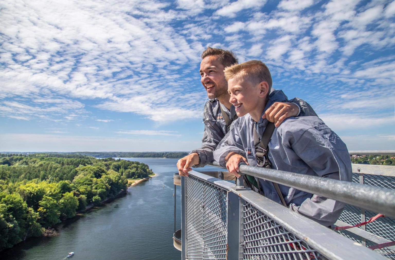 en man och en pojke står på toppen av en bro med utsikt över en flod