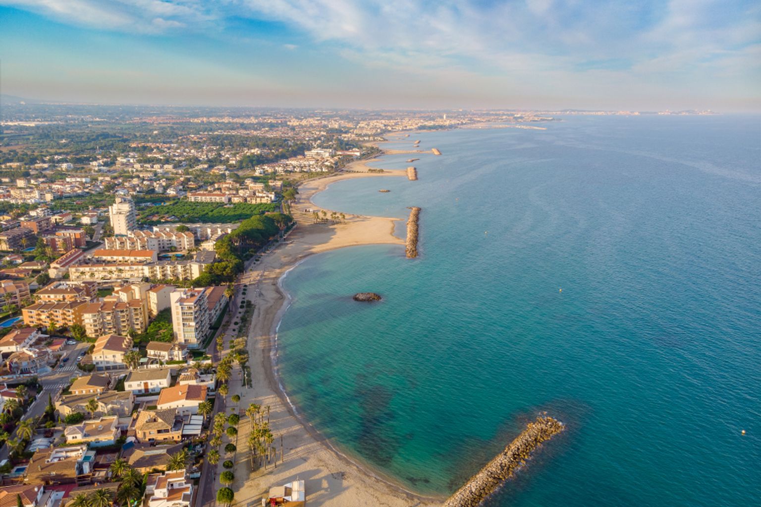 Vue aérienne d'une ville côtière avec des plages, une eau turquoise et des jetées rocheuses.