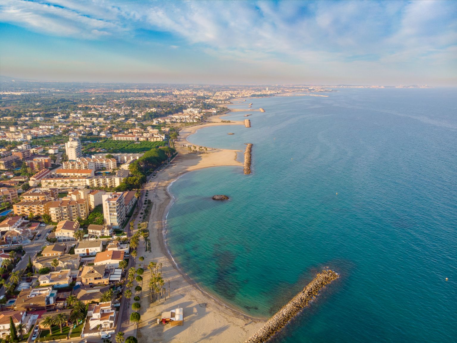 Vue aérienne d'une ville côtière avec des plages, une eau turquoise et des jetées rocheuses.