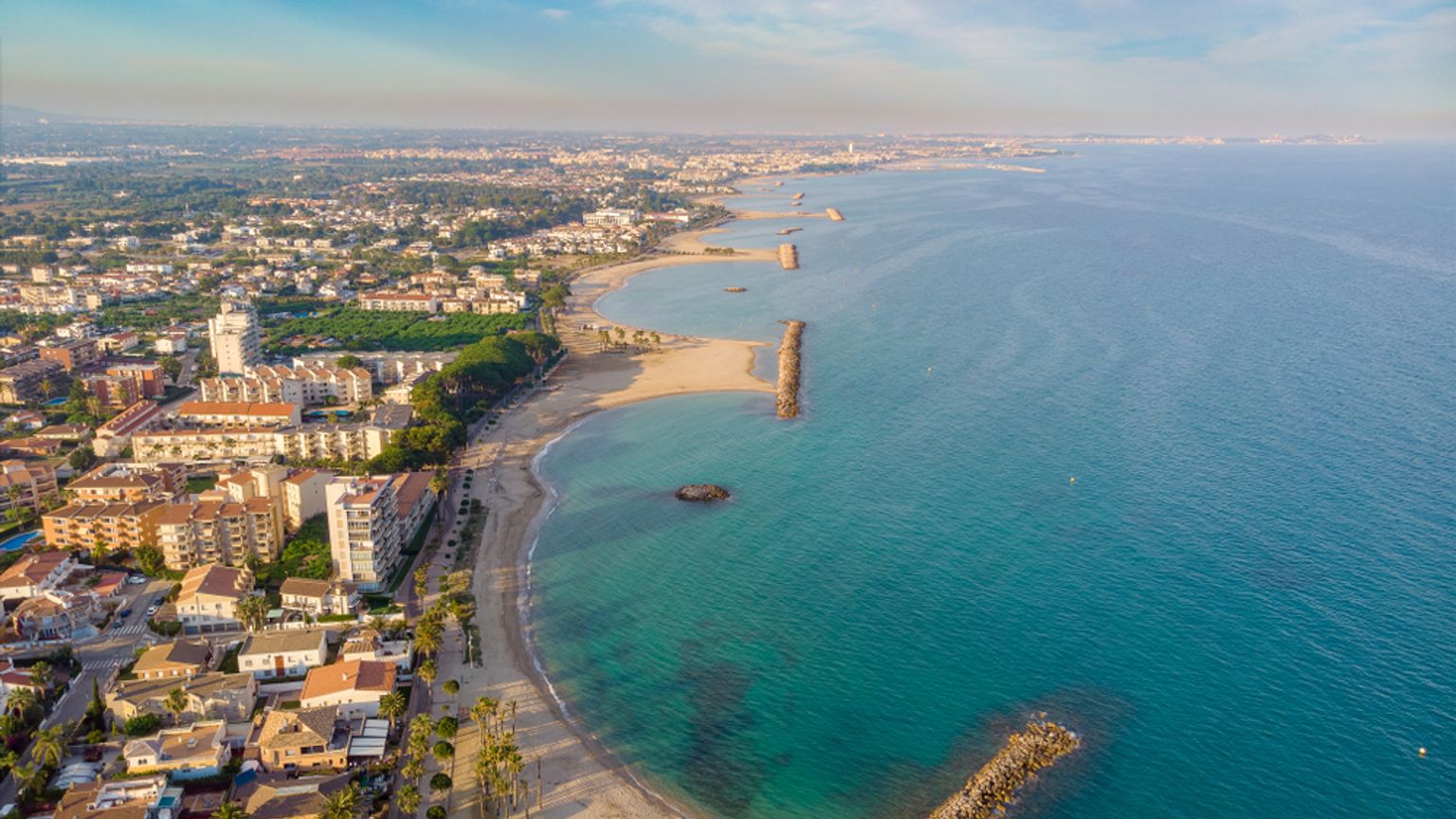 Vue aérienne d'une ville côtière avec des plages, une eau turquoise et des jetées rocheuses.