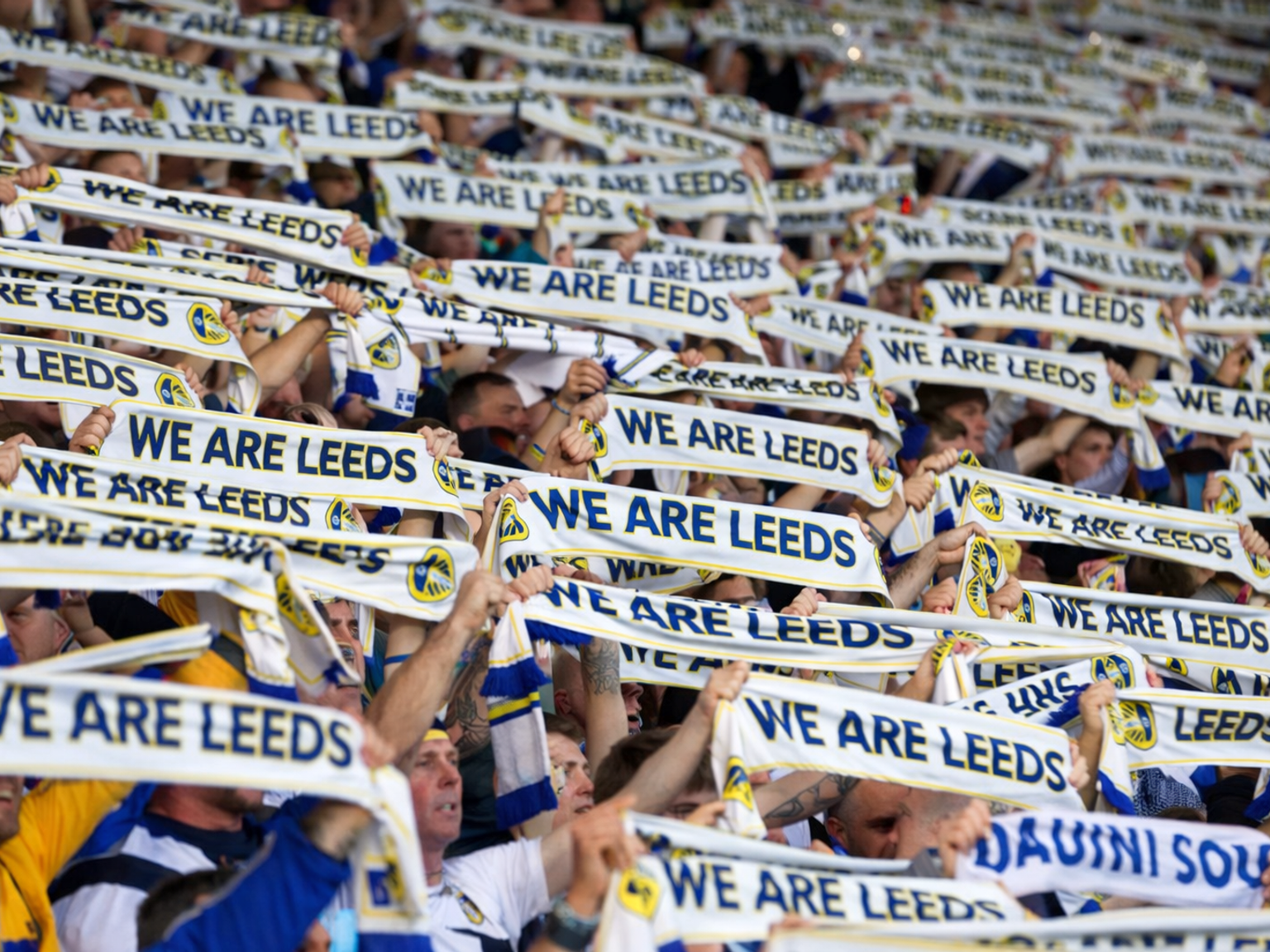 Torcedores do Leeds United segurando cachecóis "NÓS SOMOS LEEDS" acima da cabeça.