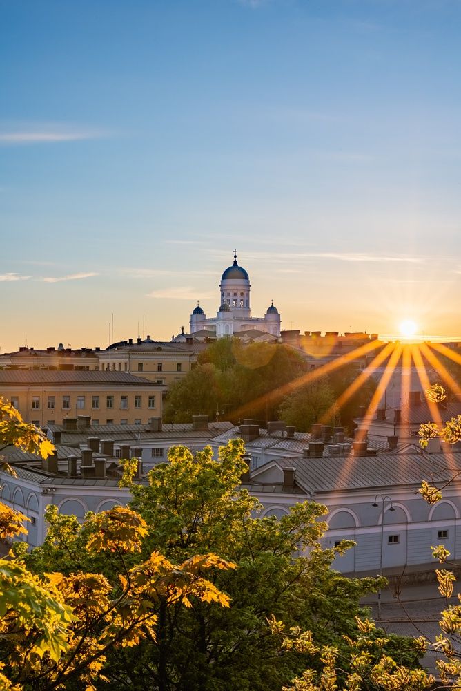 Helsinki domkirke ved solnedgang, med gyllent lys over byen og trærne.