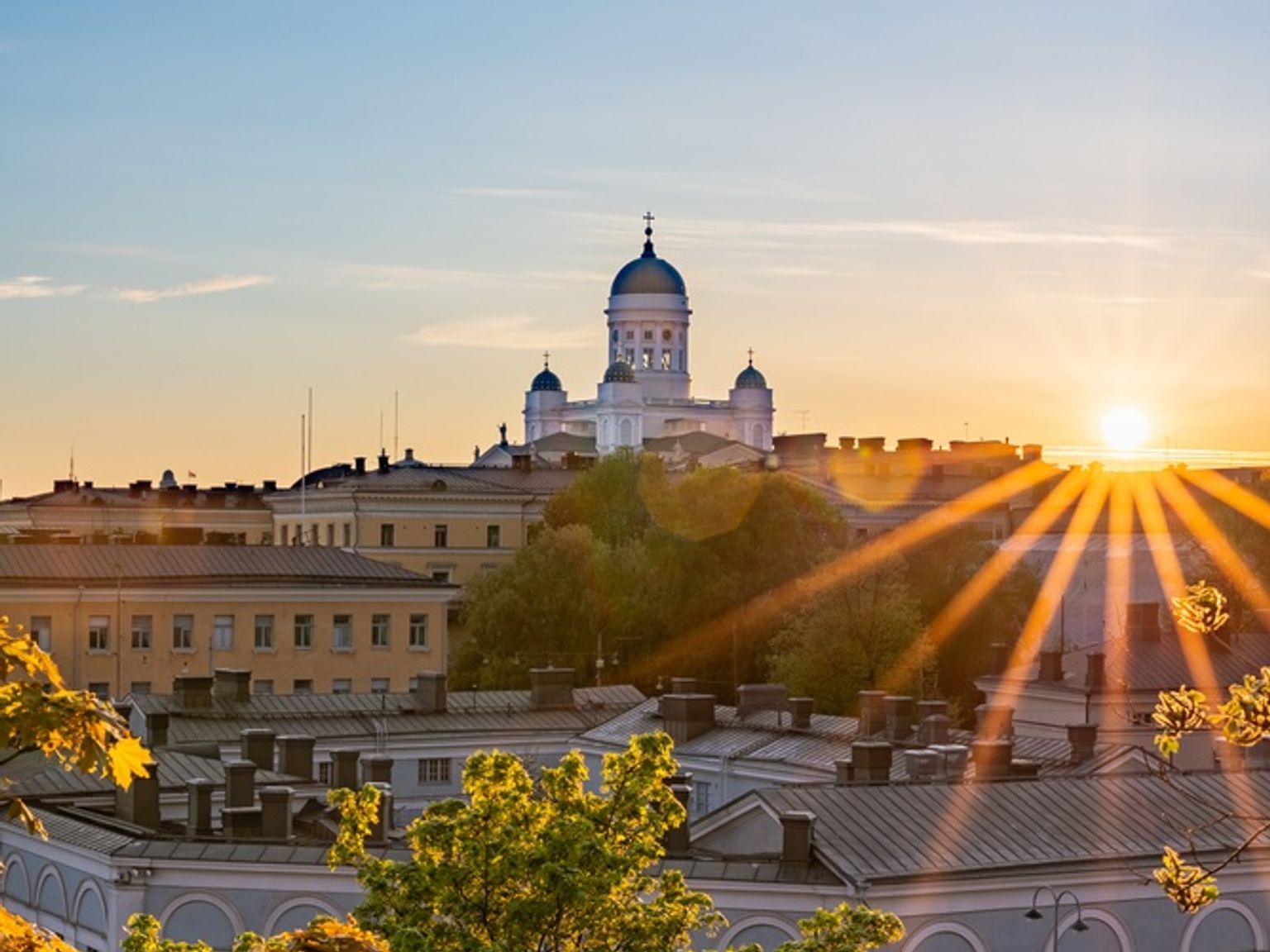 Helsinki domkirke ved solnedgang, med gyllent lys over byen og trærne.