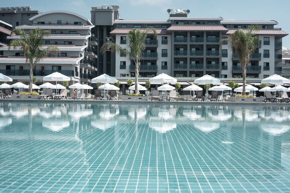 Resort swimmingpool, der reflekterer moderne bygninger, liggestole med hvide parasoller og palmetræer. Green Garden Resort & Spa Hotel, Alanya