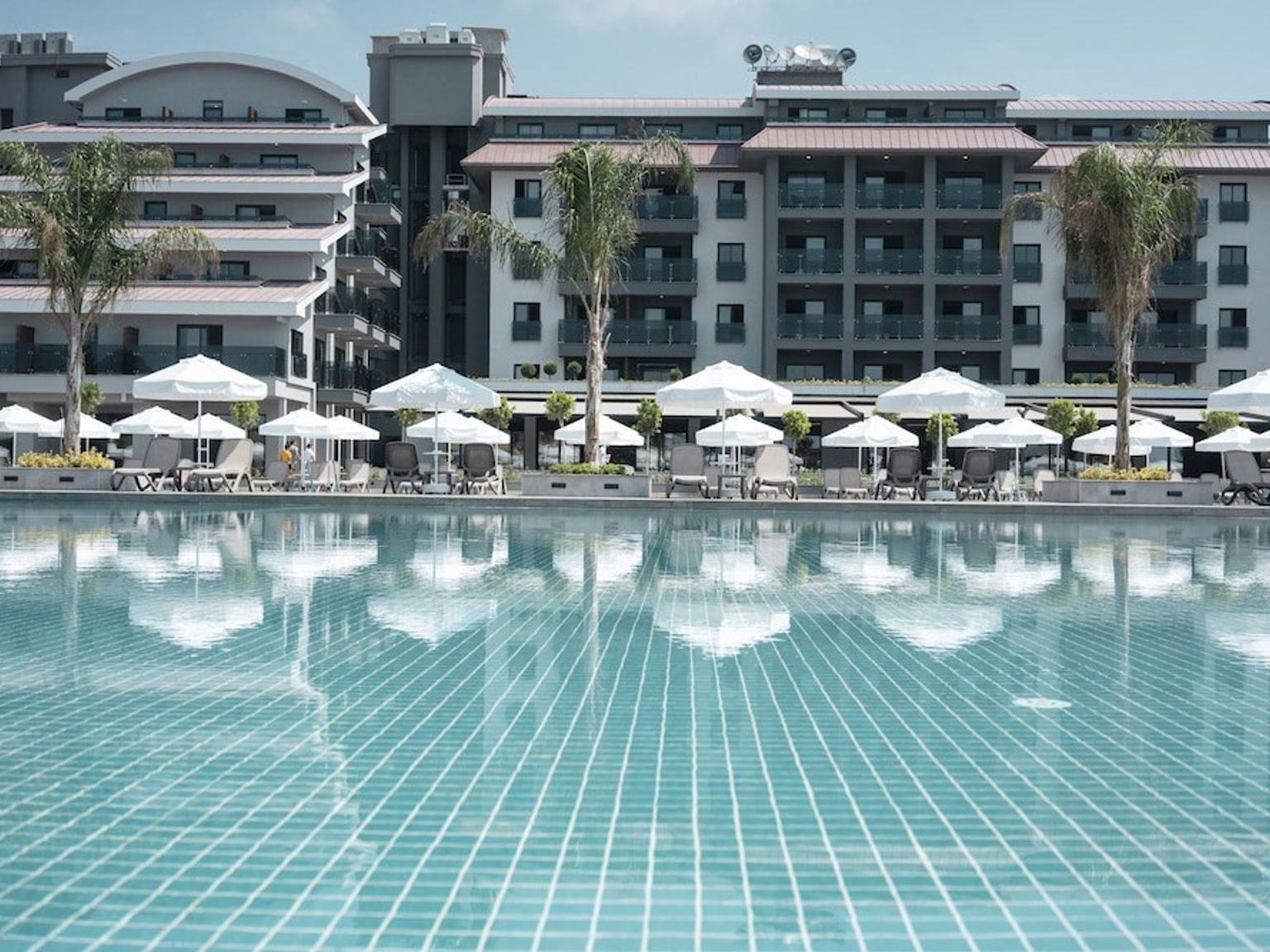 Resort swimmingpool, der reflekterer moderne bygninger, liggestole med hvide parasoller og palmetræer. Green Garden Resort & Spa Hotel, Alanya