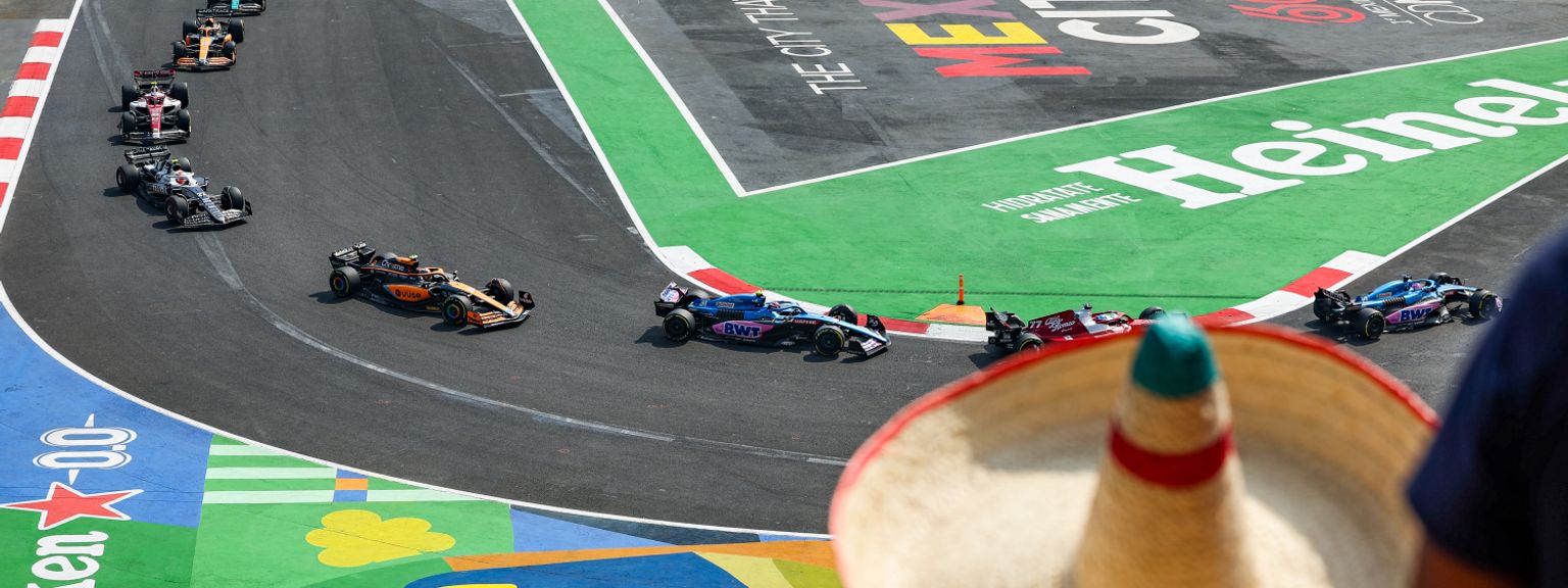 Formel 1-biler på en bane med "Mexico City" og "Heineken" logoer, sett over en tilskuerens sombrero.