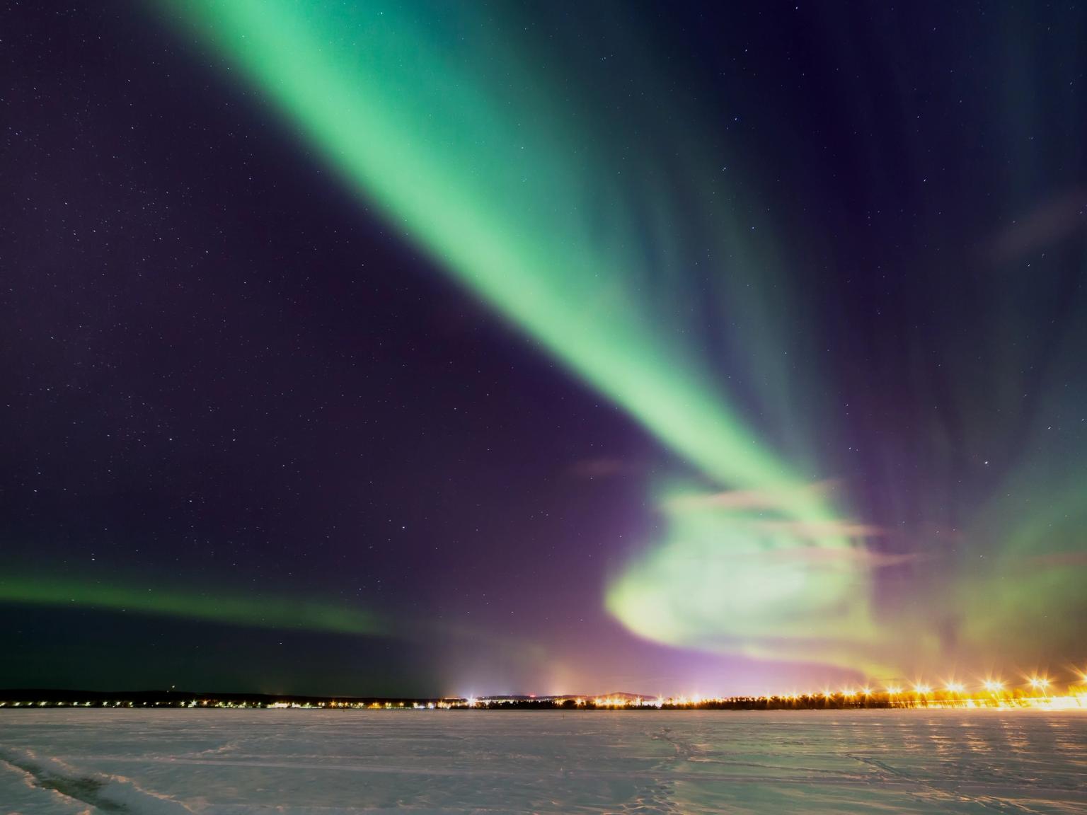 das Nordlicht tanzt im Nachthimmel über einem verschneiten Feld