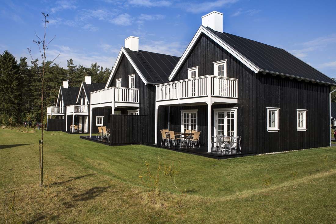 En rekke identiske svarte trehus med hvite detaljer og balkonger på en grønn plen ved siden av en skog.