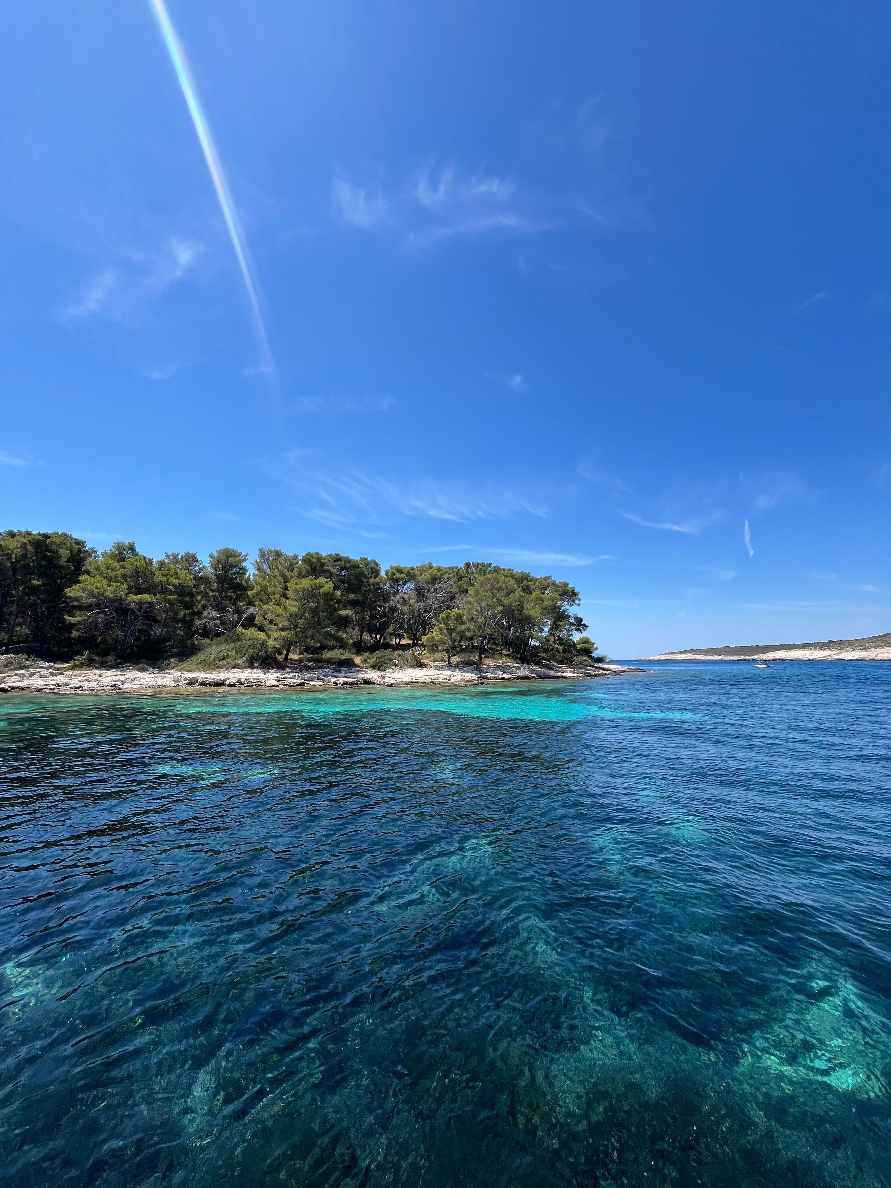Eaux turquoise cristallines au bord d’une île boisée en Croatie sous un ciel bleu éclatant.