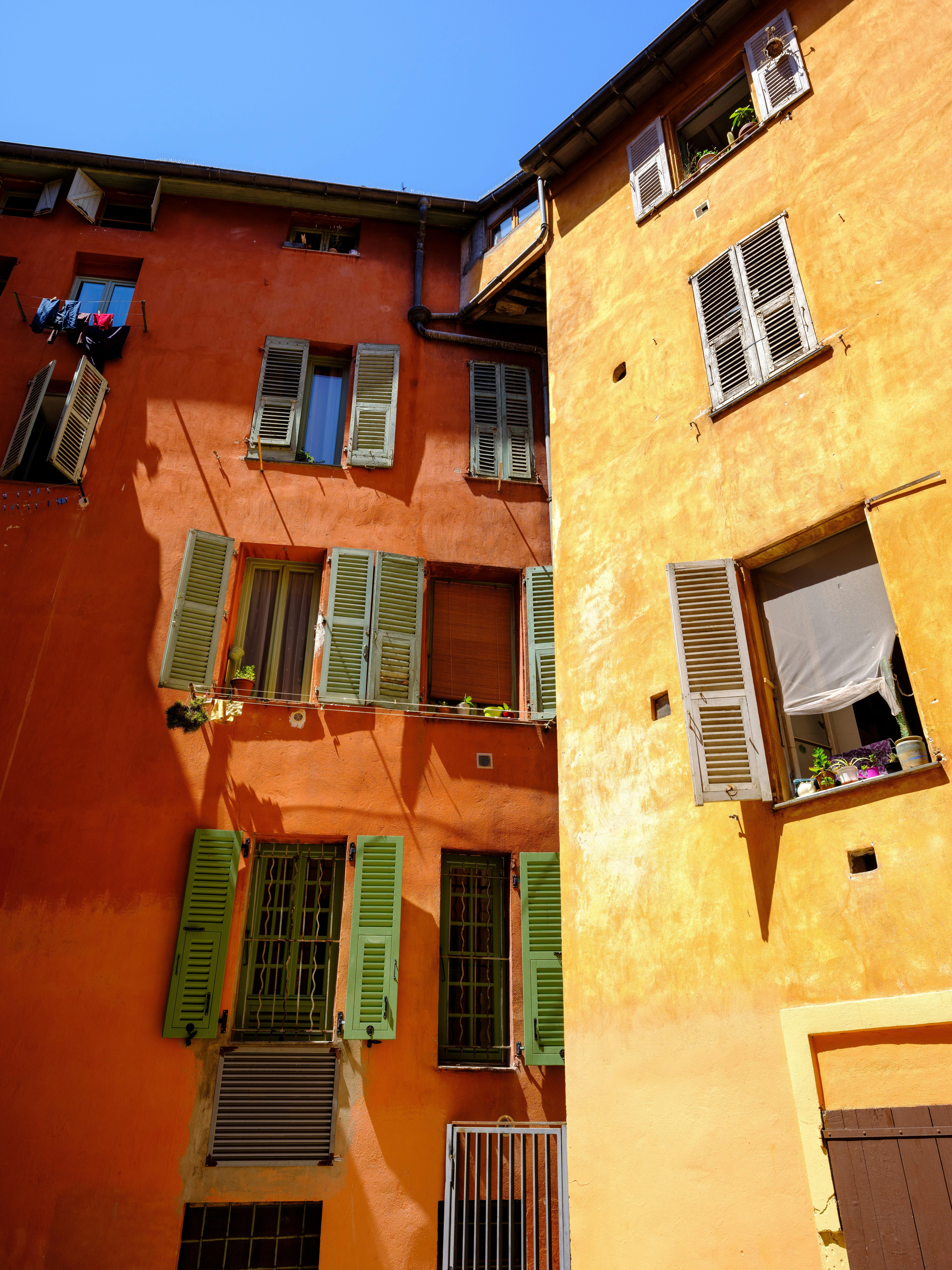 Sunlit orange and yellow buildings with many windows, shutters, and clothes drying from one window. Nice, France