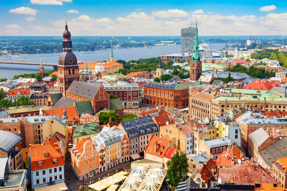 Luftfoto af en historisk europæisk by med farverige bygninger, en flod og markante kirkespir.