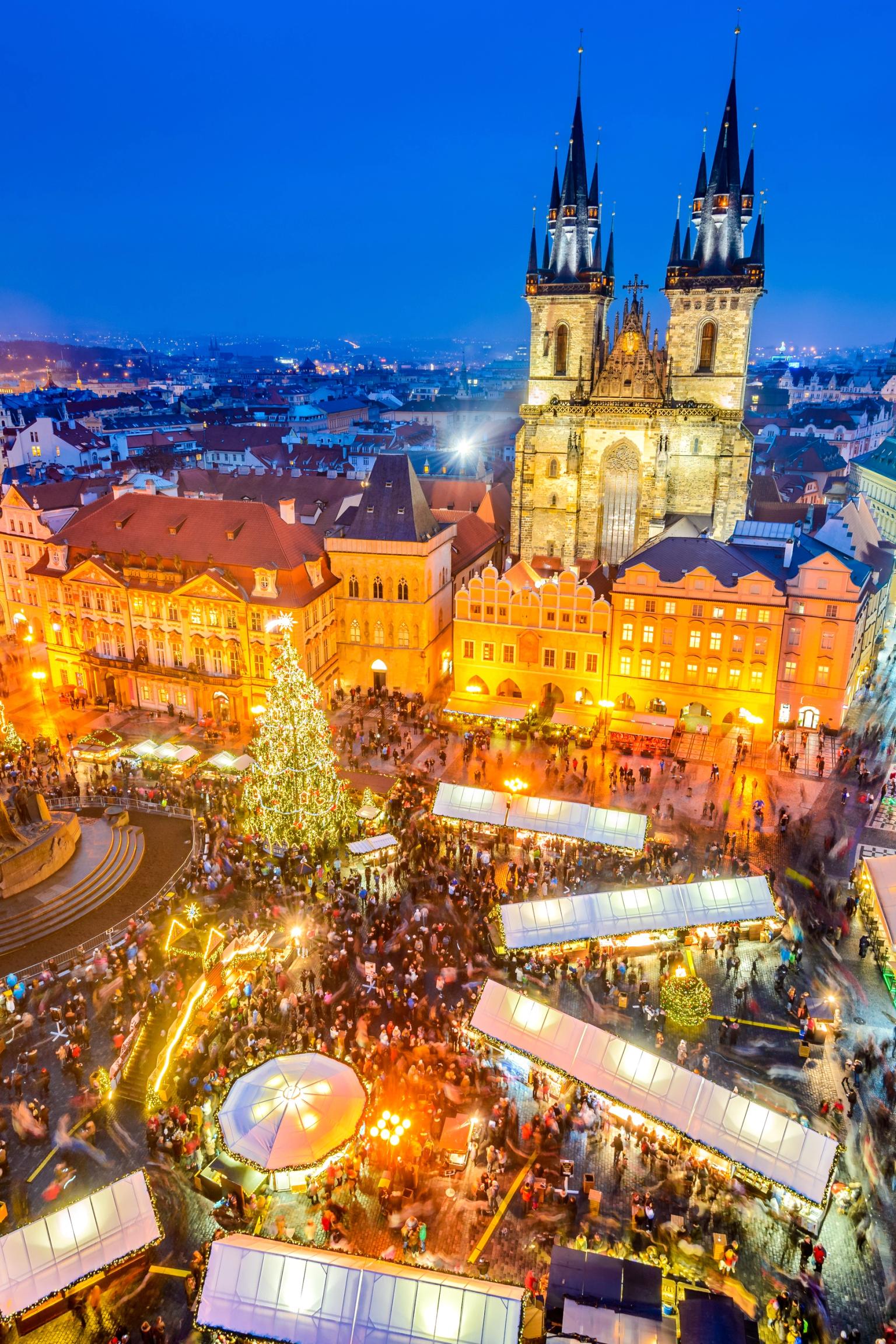 Prags gamlebytorget julemarked i skumringen, med et opplyst tre og Týn-kirken.