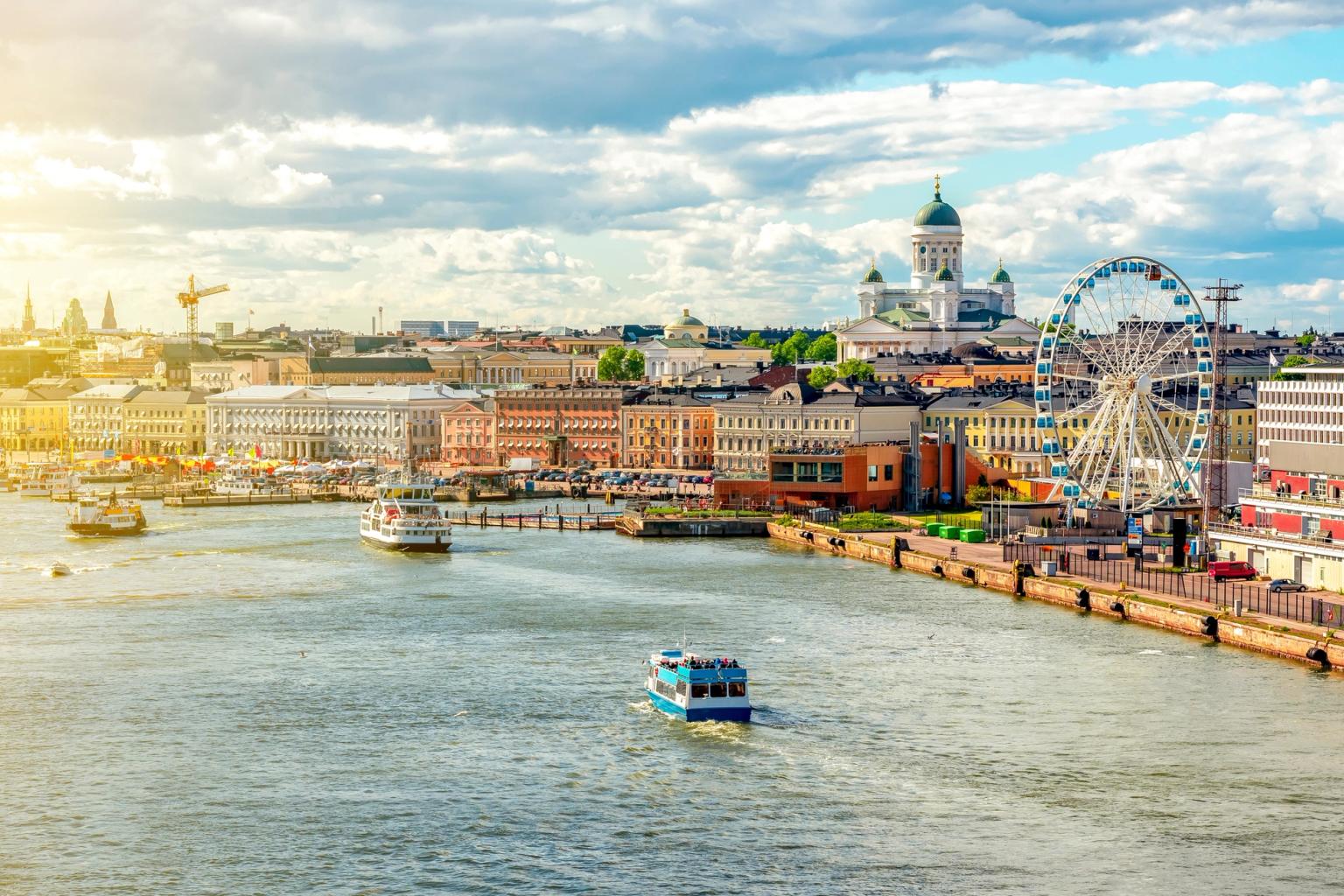 Helsinkis havneområde med båter, den hvite katedralen, et pariserhjul og fargerike bygninger under en solrik himmel.